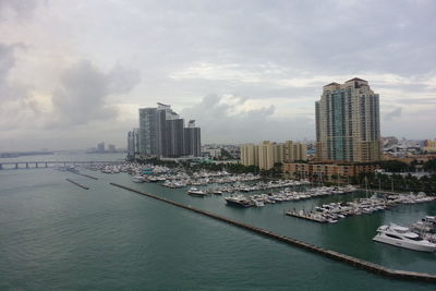 Sailboats moored at harbor by city against sky