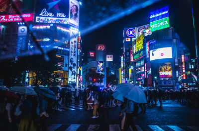 People walking on illuminated street during rainy season at night