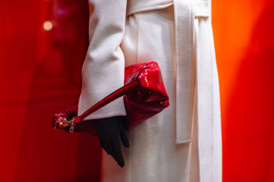 Fancy details of a classic white long coat with a belt and a patent red handbag. women's fashion