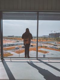 Rear view of man standing by glass window in city