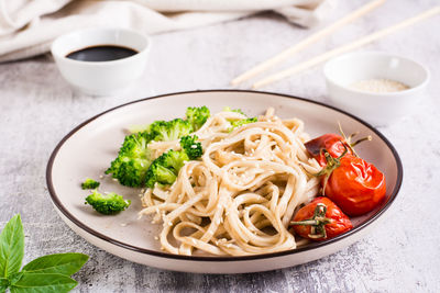 Wheat udon noodles in soy sauce with tomatoes and broccoli on a plate on the table