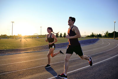 Athletes running together on track with sunset behind