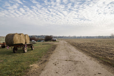 Road passing through field against cloudy sky