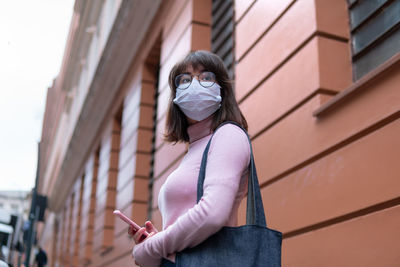 Young woman wearing mask looking away against wall