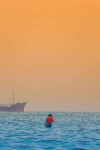 Sailboat in sea against orange sky