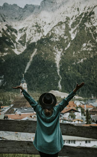 Rear view of woman with arms raised standing against mountain in town