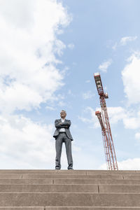 Senior businessman standing on stairs besides construction crane