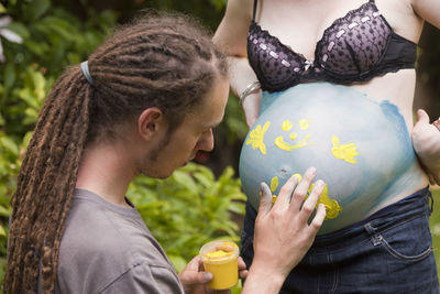 Man painting on abdomen of pregnant woman in back yard