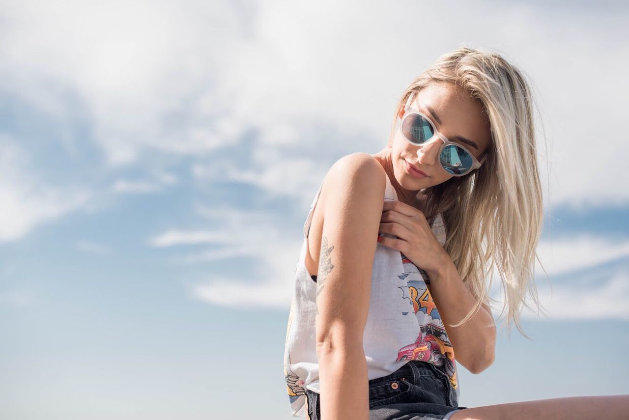 young adult, one person, smiling, blond hair, happiness, sunglasses, young women, looking at camera, leisure activity, front view, portrait, outdoors, sky, real people, beautiful woman, day, fun, enjoyment, lifestyles, cheerful, vacations, nature, standing, beauty, sea, one young woman only, people, adult, adults only