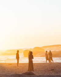 People standing on beach against sky during sunset
