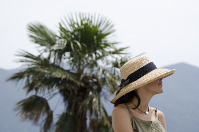 Woman wearing straw hat with palm tree in background