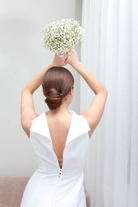 Back view of unrecognizable woman with  hairstyle in wedding dress with arms raised holding bouquet