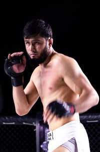 Young man looking away while standing against black background