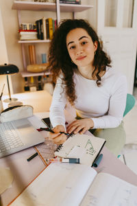 Portrait of young woman with curly hair studying while doing homework at desk