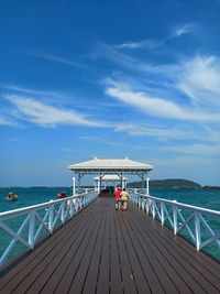 Rear view of couple walking on pier over sea