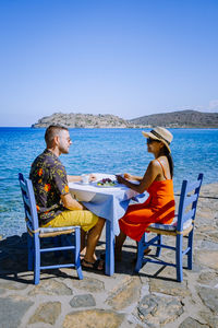 People sitting on chair at beach against clear sky