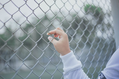 Midsection of child holding chainlink fence