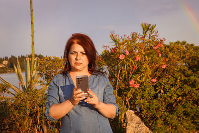 Portrait of young woman using phone while standing on plants