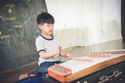 Boy playing yangqin against blackboard