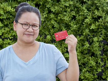 Portrait of woman holding credit card against trees