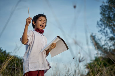 Happy boy holding umbrella on field against sky