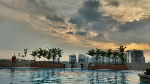 Swimming pool by buildings against sky during sunset