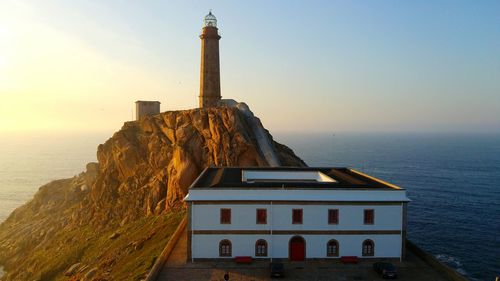 Lighthouse by sea against sky during sunset