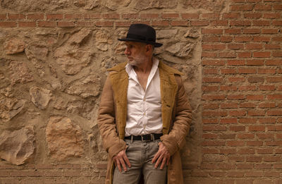 Portrait of adult man in hat and coat against yellow wall on street