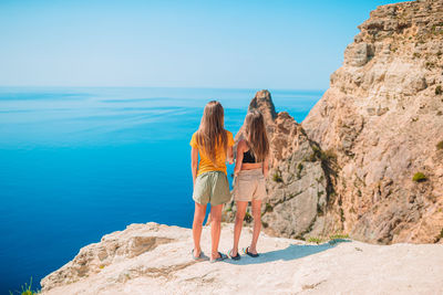 Rear view of woman looking at rock formation by sea against sky