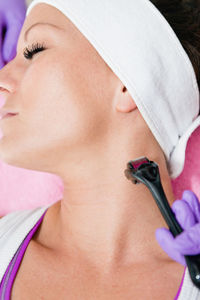 Close-up of woman lying down with while beautician using cosmetic roller on face at spa