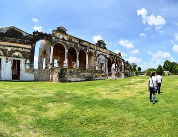 People walking on grass in front of historical building against sky