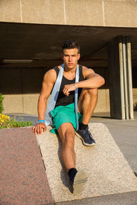 Portrait of fit young man sitting on retaining wall in city