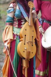 A medieval female minstrel holding her vielle next to a drummer during a festival.