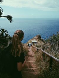 High angle view of woman standing on steps leading towards sea against sky