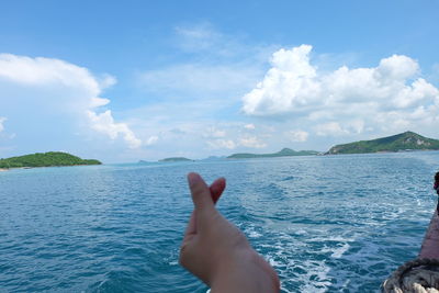 Person hand by sea against sky