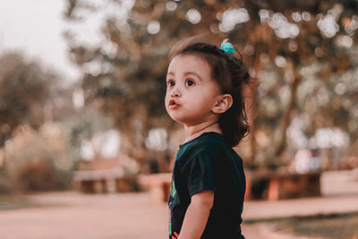 Cute girl looking away against trees