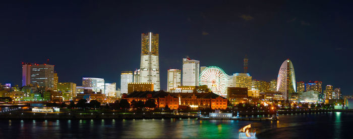 Illuminated buildings by river against sky at night