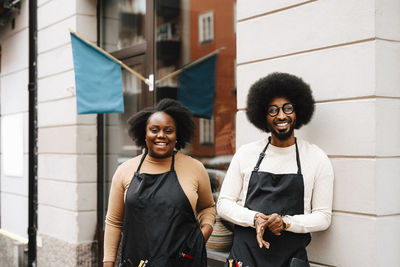 Smiling male and female coworkers standing outside barber shop