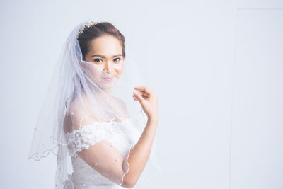 Portrait of a smiling young woman standing against white wall