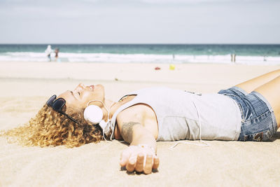 Woman listening music while lying at beach during summer