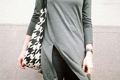 Midsection of woman with shoulder bag standing against wall