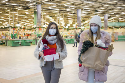 Young women in medical mask shopping for christmas in mall. xmas holidays in new covid-19 reality.