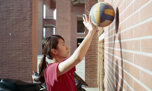Side view of young woman playing with ball on wall