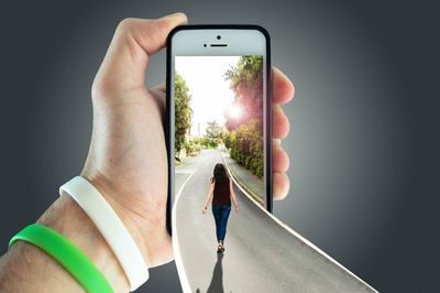 Digital composite image of woman walking on road in mobile phone