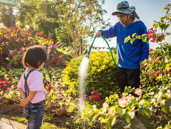 Girl standing in front of man watering plant in park