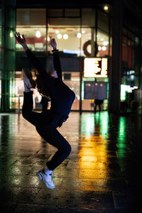 Side view of woman dancing on wet street at night