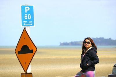 Woman standing by road signs against sky