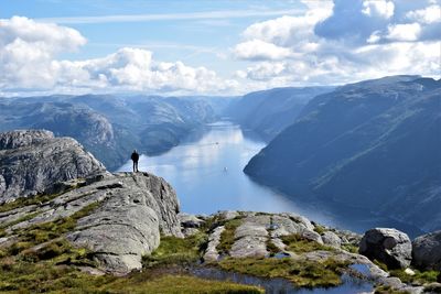 Man standing on cliff by mountains against sky