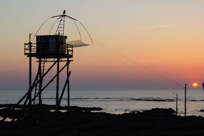 Silhouette cranes on beach against sky during sunset