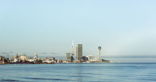 Sea and buildings in city against clear sky